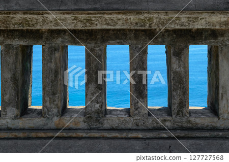 Blue Indian ocean visible through old ancient temple wall in Bali island, Indonesia. Wall is in camera focus Blue Indian ocean visible through old ancient temple wall in Bali island, Indonesia. Wall is in camera focus 127727568