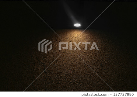 Lonely lamp illuminating brown concrete wall in absolute darkness Lonely lamp illuminating brown concrete wall in absolute darkness 127727990