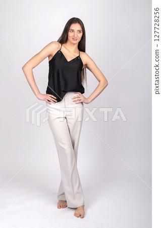 Beautiful woman with black blouse and white pants studio portrait 127728256