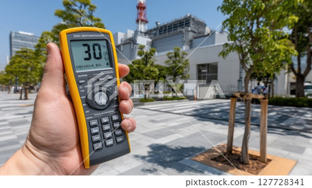 Hand displays a radiation counter reading 3.0, highlighting safety measures near a nuclear facility on a bright day 127728341