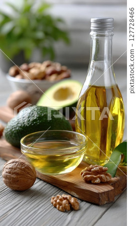 Half an avocado rests beside walnuts and hazelnuts next to a glass of liquid plant-based oil on a rustic wooden table Half an avocado rests beside walnuts and hazelnuts next to a glass of liquid plant-based oil on a rustic wooden table 127728466