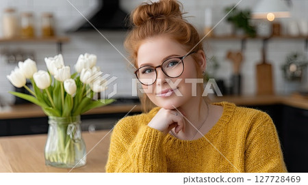 Smiling woman in a yellow top eats a nutritious salad at her kitchen table near vibrant tulips, embracing a healthy lifestyle 127728469
