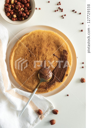 Crepes with chocolate hazelnut spread, strawberries and hazelnuts on a white wooden table. Top view 127729338