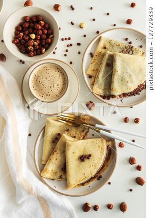 Crepes with chocolate hazelnut spread, strawberries and hazelnuts on a white wooden table. Top view 127729339