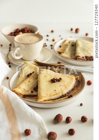 Crepes with chocolate hazelnut spread, strawberries and hazelnuts on a white wooden table. Crepes with chocolate hazelnut spread, strawberries and hazelnuts on a white wooden table. 127729340