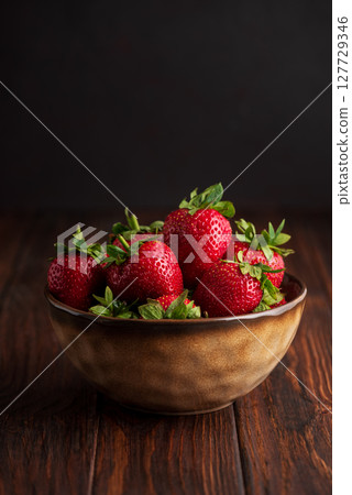 Fresh red strawberries in a rustic bowl on a dark wooden background. Front view Fresh red strawberries in a rustic bowl on a dark wooden background. Front view 127729346