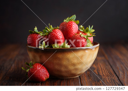 Fresh red strawberries in a rustic bowl on a dark wooden background. Front view Fresh red strawberries in a rustic bowl on a dark wooden background. Front view 127729347