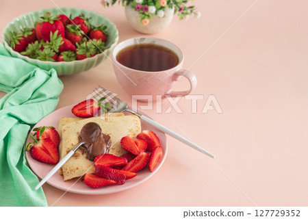 Crepes with chocolate spread and fresh strawberries, served with tea on pink background 127729352