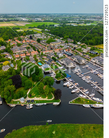A top-down view of a marina with multiple boats docked along wooden piers, a boat cruising through a narrow waterway surrounded by green parks and natural grassy areas. A top-down view of a marina with multiple boats docked along wooden piers, a boat cruising through a narrow waterway surrounded by green parks and natural grassy areas. 127729523
