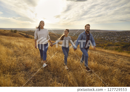Happy smiling family with child girl walking in the field enjoying nature together. 127729553