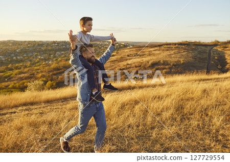 Portrait of little child boy sitting on fathers shoulders enjoying sunset and nature outdoors. Portrait of little child boy sitting on fathers shoulders enjoying sunset and nature outdoors. 127729554