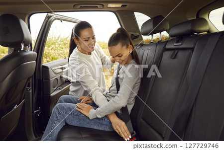Young smiling mother fastening with seat belt her teenage daughter sitting inside a car. 127729746