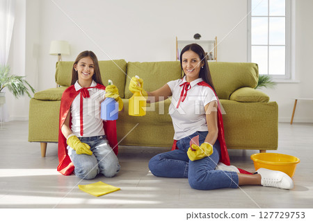 Happy smiling mother with child daughter in super heroes costumes cleaning floor at home. 127729753