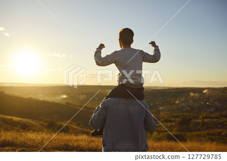 Child boy sitting on fathers shoulders and looking into the distance enjoying sunset outdoors 127729785