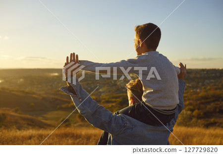 Portrait of son sitting on fathers shoulders and looking into the distance during a walk in nature. 127729820