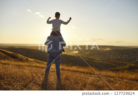 Little child boy walking with father sitting on his shoulders and enjoying nature outdoors. 127729824