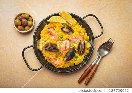 Spanish seafood Paella with shrimps, mussels, peas and lemon in a pan on light beige background top view 127730022