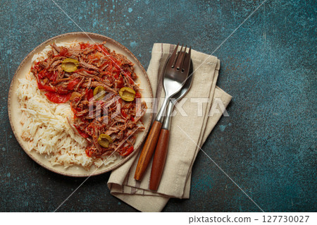 Ropa vieja with white rice, tomato sauce and green olives on a plate top view, traditional dish of Cuba 127730027