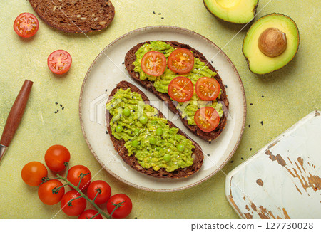 Healthy breakfast with avocado, tomatoes and peas on rye bread top view on light green background 127730028