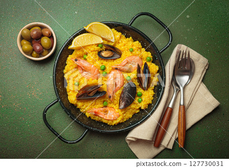 Spanish seafood Paella with shrimps, mussels, peas and lemon in a pan on green rustic background top view 127730031