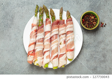 Fresh asparagus wrapped in bacon with peppercorns on gray concrete background top view 127730043