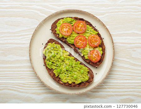 Healthy avocado toast with green peas and cherry tomatoes on whole rye bread top view on white wooden background Healthy avocado toast with green peas and cherry tomatoes on whole rye bread top view on white wooden background 127730046