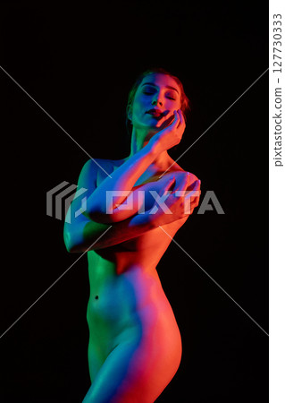 Model poses gracefully with artistic lighting against black backdrop Model poses gracefully with artistic lighting against black backdrop 127730333