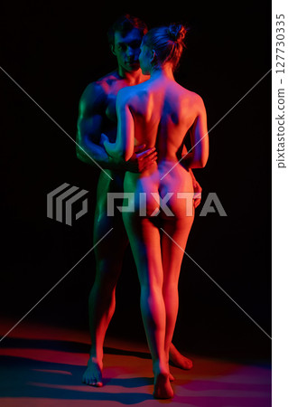 Couple posing sensually in colorful lighting with artistic shadow play 127730335