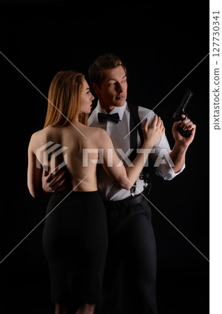 Dramatic interaction between a couple in evening attire with a firearm 127730341
