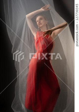Dynamic woman expressing emotion in elegant red dress with soft drapery in a studio setting Dynamic woman expressing emotion in elegant red dress with soft drapery in a studio setting 127730345