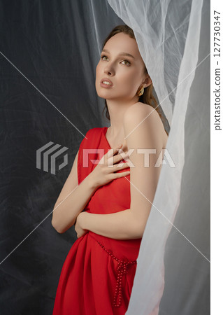 Woman poses gracefully in a studio setting, expressing deep emotion while draped in a red dress 127730347