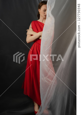 Woman in a red dress poses in a studio, showcasing a range of emotions against a dark background Woman in a red dress poses in a studio, showcasing a range of emotions against a dark background 127730348
