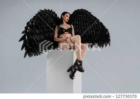 Woman poses confidently in black lingerie with striking wings 127730370