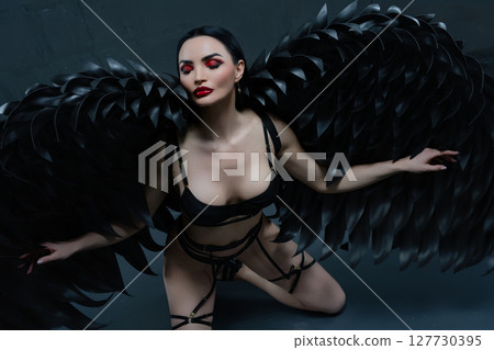Woman in black lingerie with striking wings posed artfully in a dramatic setting 127730395