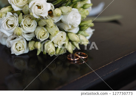 Wedding rings and white rose bouquet on dark wooden table in warm indoor lighting Wedding rings and white rose bouquet on dark wooden table in warm indoor lighting 127730773