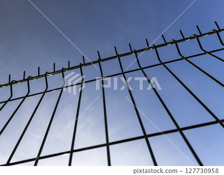 a thin metal lattice fence against a blue sky background, a small thin fence dividing the territory against a cloudless sky 127730958