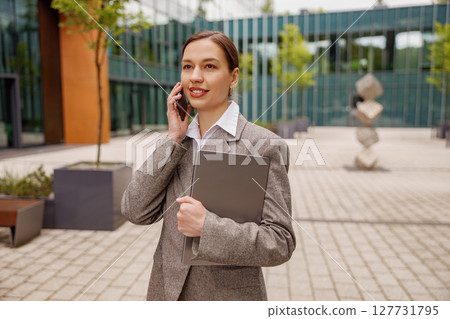 Professional businesswoman engaged in a phone conversation outside a modern urban building Professional businesswoman engaged in a phone conversation outside a modern urban building 127731795