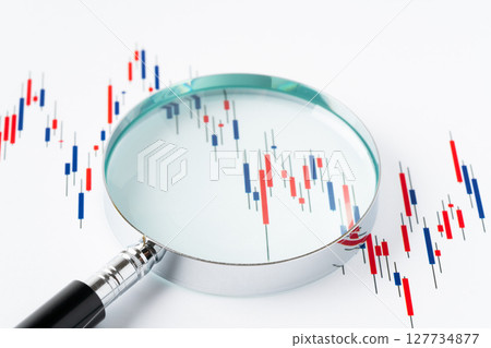 Candlestick chart magnified with a magnifying glass on a white background 127734877