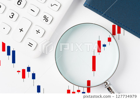A rising candlestick chart magnified with a magnifying glass 127734979