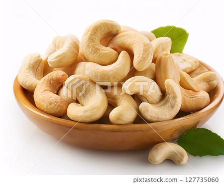 A wooden bowl filled with golden cashews, with a few cashews scattered around and green leaves A wooden bowl filled with golden cashews, with a few cashews scattered around and green leaves 127735060