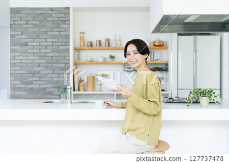 Middle woman using a tablet in the kitchen Middle woman using a tablet in the kitchen 127737478