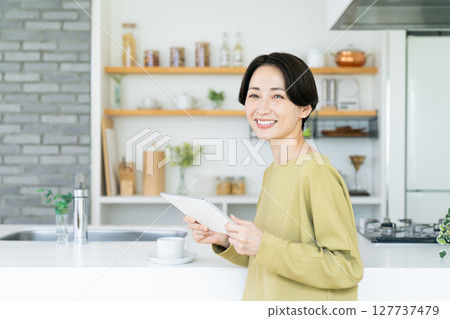 Middle woman using a tablet in the kitchen Middle woman using a tablet in the kitchen 127737479