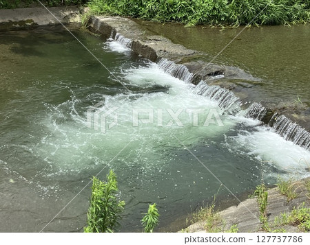 Water flowing through a small weir and white splashes 127737786