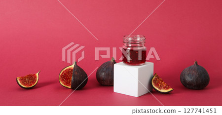 Figs and jar of jam on white block on pink background 127741451