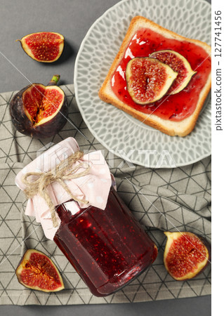 Figs, jars of jam, towel and bread with jam on plate on gray background, top view 127741456