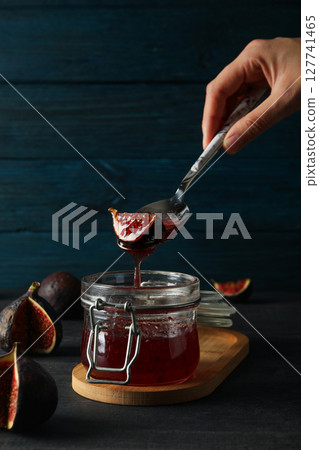 Jar of jam and spoon with figs in hand on blue wooden background Jar of jam and spoon with figs in hand on blue wooden background 127741465