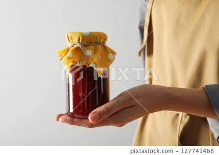 Jar with fig jam in hand on white background 127741468