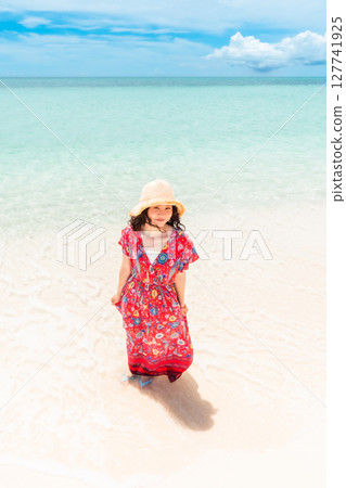 A young woman in a dress walking along the water's edge on a tropical beach 127741925