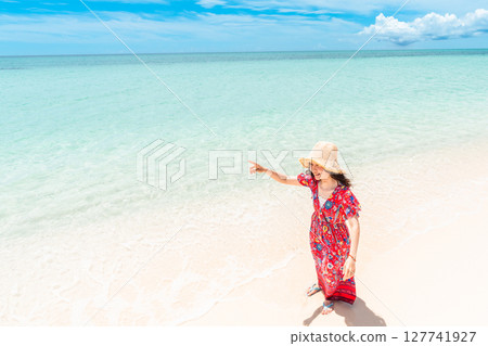 一位身穿洋裝的年輕女子在熱帶海灘的水邊散步 一位身穿洋裝的年輕女子在熱帶海灘的水邊散步 127741927