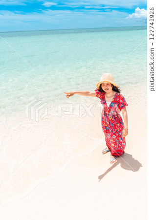 A young woman in a dress walking along the water's edge on a tropical beach 127741928